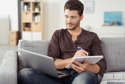 young man looking at laptop and taking notes
